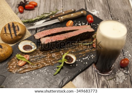 Ribeye steak from marble beef meat with vegetables and barbecue sauce. Served on a plate of black stone with fork and knife and beer.