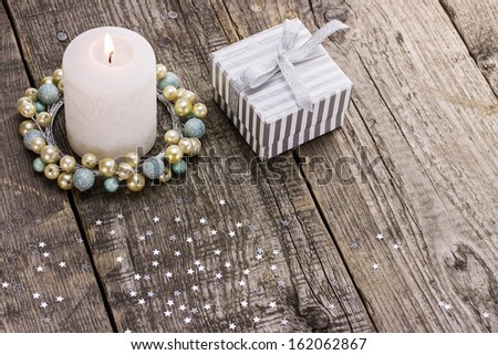 Burning Christmas candle and gift box on wooden background