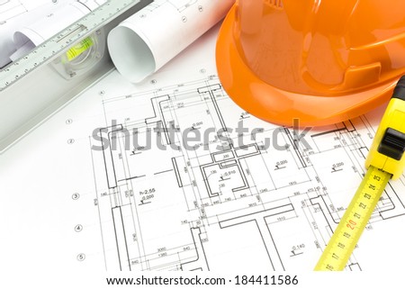 Safety orange helmet with level and tape measure over project drawings
