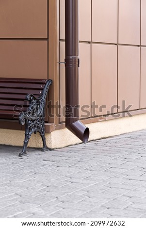 Corner of building with metal drainpipe and ornate bench