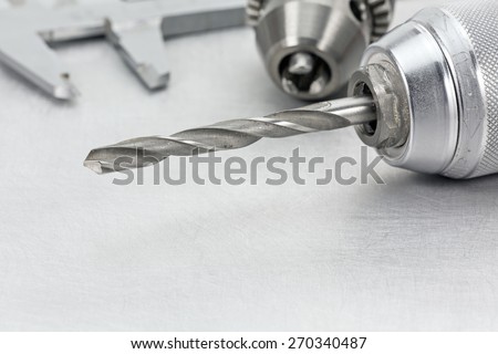 Electric drill chuck with drill bits and vernier caliper on metal background