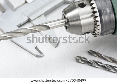 Electric drill head with drill bits and vernier caliper on scratched metal background