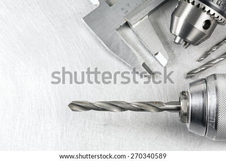 Power drill head with drill bits and vernier caliper on scratched metal background