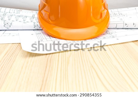 safety helmet, blueprints and construction plans on wooden background