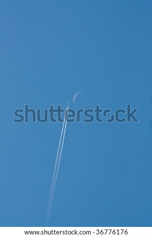 Airplane with contrails against the blue sky and the early moon