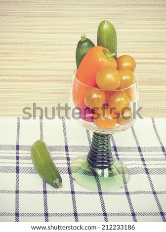 Snack vegetables cherry tomatoes, bell peppers and cucumbers in a stem glass on table. Toned photograph in a nostalgic retro style.