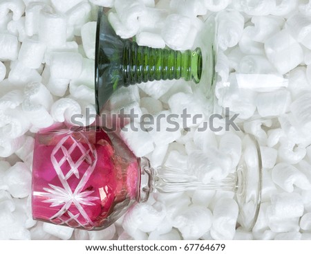 Two wine glasses, red and green, in packing peanuts