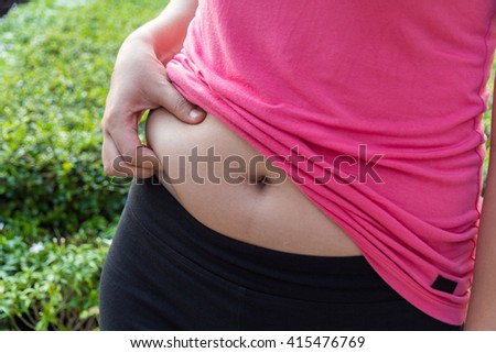 woman hand holding belly fat in the park concept