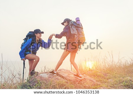 Hiker women helping her friend climb up the last section of sunset in mountains. Traveler teamwork in outdoor lifestyle adventure and camping. Travel Concept.