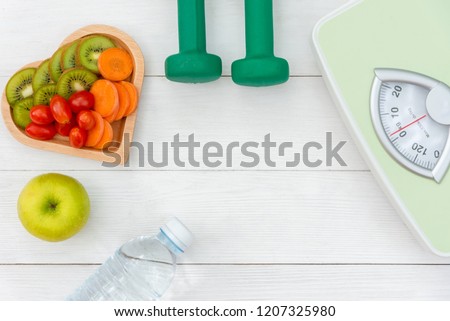 Diet and weight loss for healthy care with  weight scale and fitness equipment,fresh water and fruit healthy, green apple, banana, carrot on white wooden background top view.  Healthy Concept.