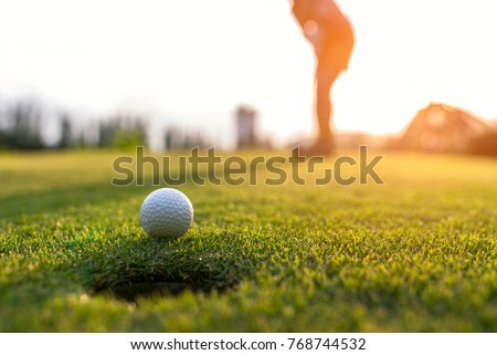 Golfer asian woman focus putting golf ball on the green golf on sun set evening time.. Healthy and Lifestyle Concept.