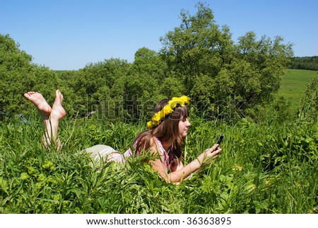 Pretty girl with smart-phone and flower\'s diadem in grass