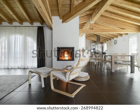armchair near to fireplace in the living room of a apartment overlooking on the dining room with wood ceiling