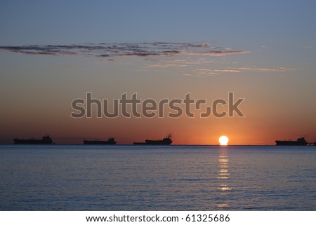 Side view of silhouetted tanker ship with orange sunset background.