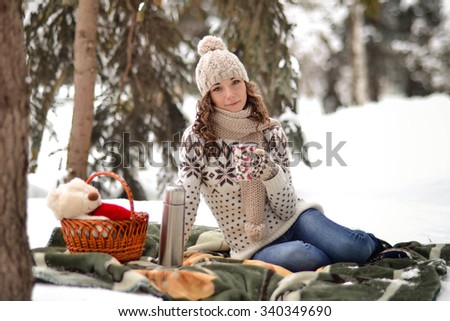 Beautiful girl sitting on a blanket in the winter in the fosest and drinking tea