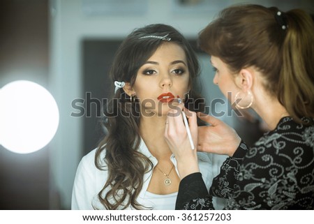 Professional expert,makeup artist prepares very beautiful,young,well-known,glamorous,stunning model for filming shooting for cover of fashion magazine VOGUE,does make-up,makes up lips,art,eyes,white.