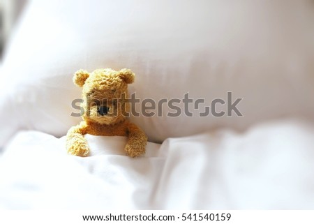 Bear is sick in bed on white pillow and white bed.