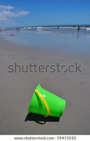 Child's green sand bucket on beach, perfect for cover art