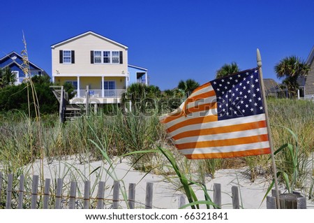 Pretty beach scene with rental home, dune and American flag.