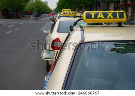 A row of three taxis waiting in line for customers on Berlin\'s Unter den Linden, TAXI sign big in right area of the frame, on a grey day