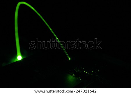 A green glowing fiber optic cable emitts light on a part of a circuit board revealing integrated-circuits