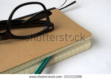 Brown notebook with black glasses and a pencil between pages, on white, closeup