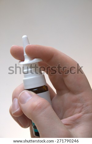 A male hand is holding a bottle of nasal spray, as commonly used with allergies, infections, or a cold