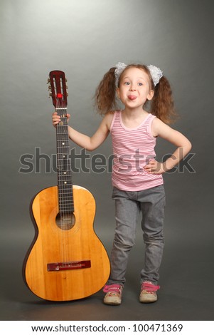 the little girl costs with a big guitar, a look not in a lens, puts out the tongue, a guitar holds for a signature stamp, a vertical shot,