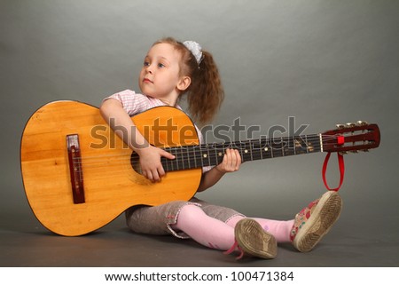 the little girl sits on a floor with a big guitar, a look not in a lens