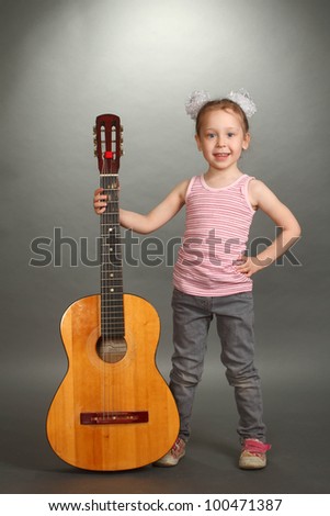 the little girl costs with a big guitar, a look not in a lens, smiles, a guitar holds for a signature stamp, a vertical shot, a double 3