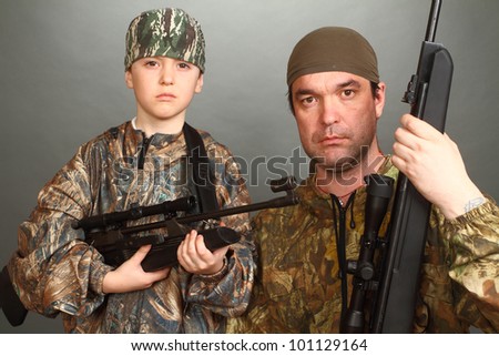 the boy and the adult man in a camouflage with rifles nearby in a shot, look in the chamber, a close up