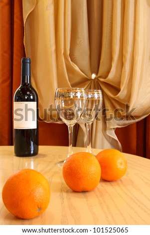 table, on a table a wine bottle, glasses and oranges, behind a curtain