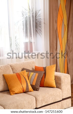 Decorative Pillows On A Beige Sofa Against A Window With A Curtain