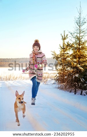 Portrait of the beautiful girl running near a dog in the winter wood