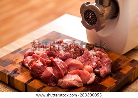 The electric meat grinder and the cut meat on a wooden chopping board