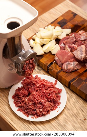 The electric meat grinder, forcemeat, onions and the cut meat on a chopping board