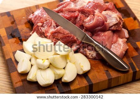 the cut meat, onions and steel knife on a wooden chopping board