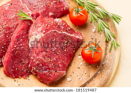 Slices of meat in salt and pepper, rosemary and tomatoes on a round plate