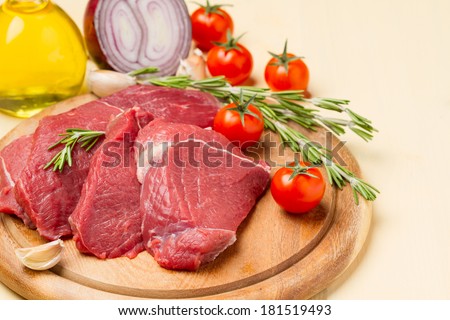 Raw meat on round board, tomatoes, onions, oil and rosemary