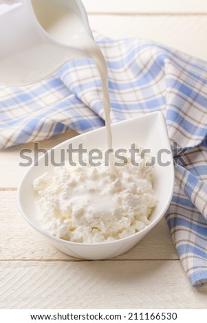 Pouring dairy cream in fresh homemade cottage cheese
