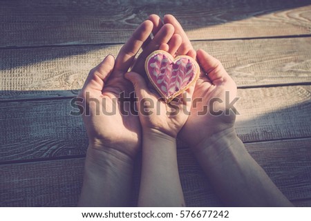 Female and children\'s hands hold cookies in the form of heart on a wooden table-top. Sunlight. A concept by the Mother\'s Day. Vintage toning.