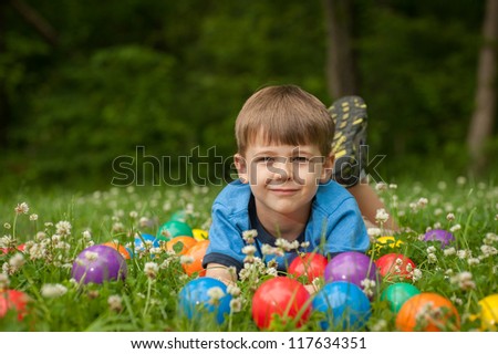 A five year old boy lays in the grass surrounded by colorful toy balls. The boy has expressions of fun and happiness.