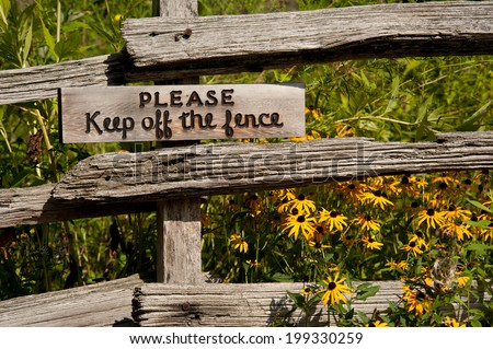 Homemade sign hanging on a split rail fence with a gentle warning to keep off the fence.