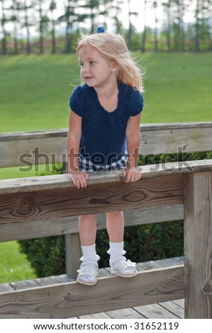 young girl looking away standing on fence