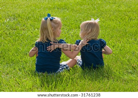 two girls sitting in the grass with arms around each other