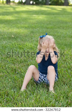 little girl sitting in grass holding hands over eyes