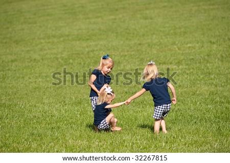 Three little girls playing in grass all three are sisters with one set of twins