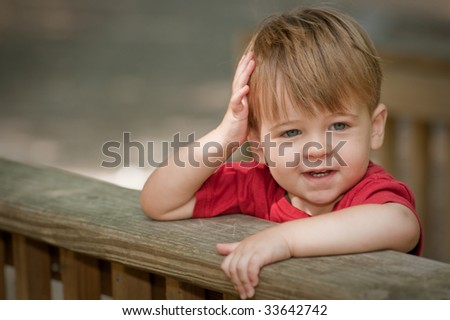 little boy looking happy with arms over deck railing and one on his head