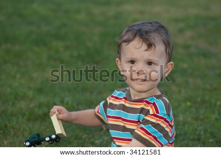 Little boy playing with toy truck looking at camera and smiling with grass in the background