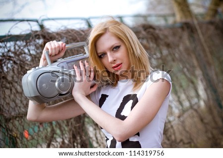Beautiful girl with tape recorder shoulder near the fence